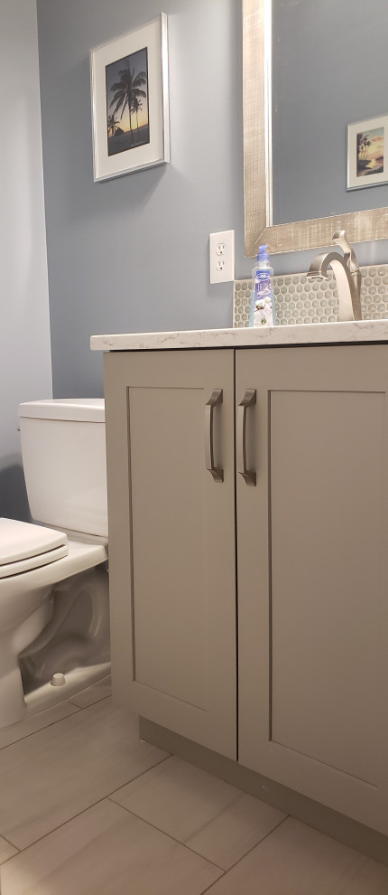 Photo of a small transitional powder room in Detroit with shaker cabinets, grey cabinets, a two-piece toilet, gray tile, glass sheet wall, blue walls, an undermount sink, engineered quartz benchtops, white benchtops and a built-in vanity.