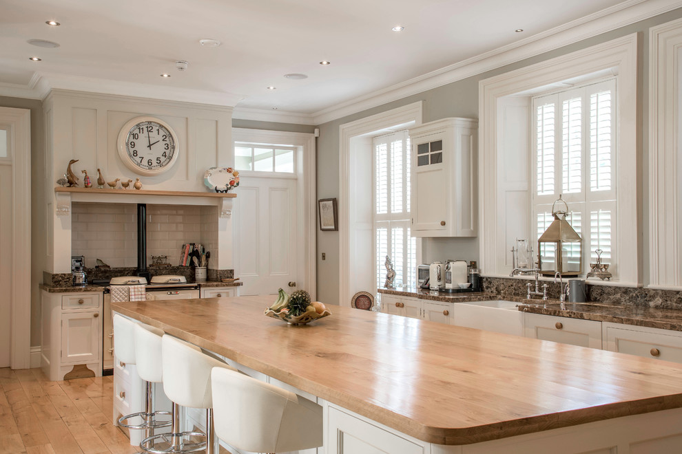 Photo of a large traditional kitchen in Belfast with a farmhouse sink, light hardwood floors, with island, beige floor, brown benchtop, shaker cabinets, grey cabinets, grey splashback and subway tile splashback.