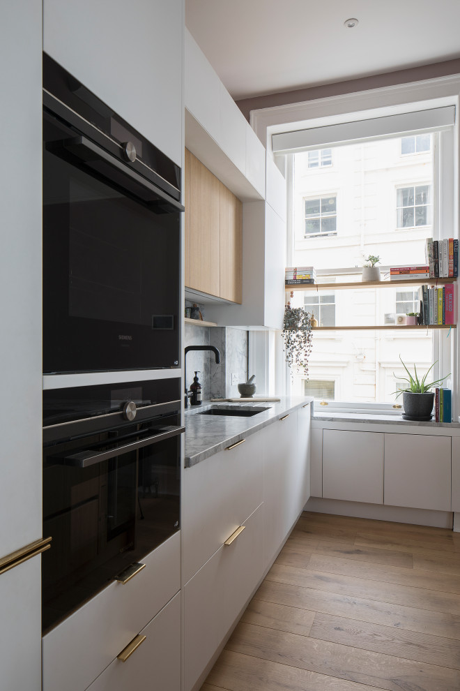 This is an example of a mid-sized scandinavian single-wall open plan kitchen in Sussex with an undermount sink, flat-panel cabinets, white cabinets, marble benchtops, grey splashback, marble splashback, panelled appliances, light hardwood floors, with island, brown floor, grey benchtop and coffered.
