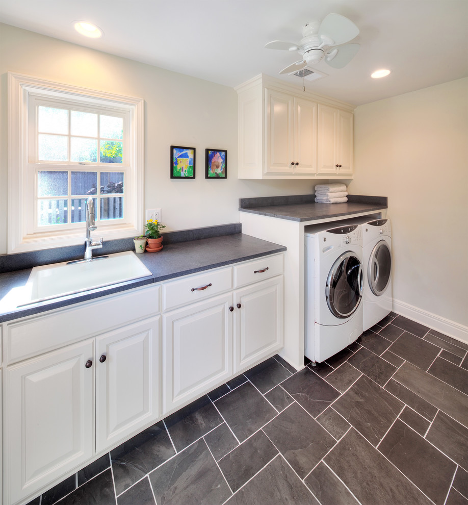 Design ideas for a large traditional single-wall dedicated laundry room in Kansas City with a drop-in sink, raised-panel cabinets, white cabinets, grey walls, porcelain floors and a side-by-side washer and dryer.
