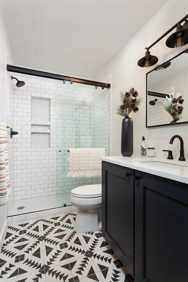 This is an example of a transitional bathroom in Denver with shaker cabinets, black cabinets, an alcove shower, white tile, subway tile, white walls, an undermount sink, multi-coloured floor, a sliding shower screen and white benchtops.