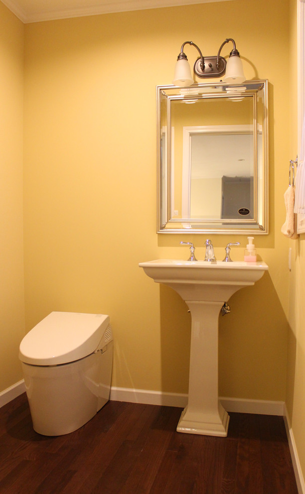 Photo of a traditional powder room in Other with yellow walls, dark hardwood floors, a console sink and brown floor.