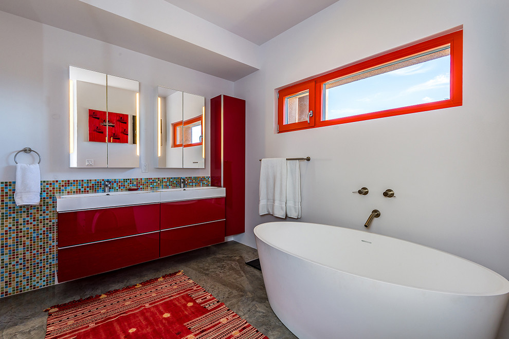 This is an example of a large contemporary master bathroom in Albuquerque with a freestanding tub, mosaic tile, flat-panel cabinets, red cabinets, white walls, concrete floors, an integrated sink, multi-coloured tile, engineered quartz benchtops, brown floor and white benchtops.