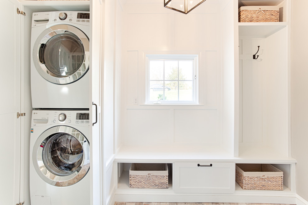 Photo of a mid-sized transitional galley utility room in Philadelphia with shaker cabinets, white cabinets, beige walls, brick floors, a stacked washer and dryer and brown floor.