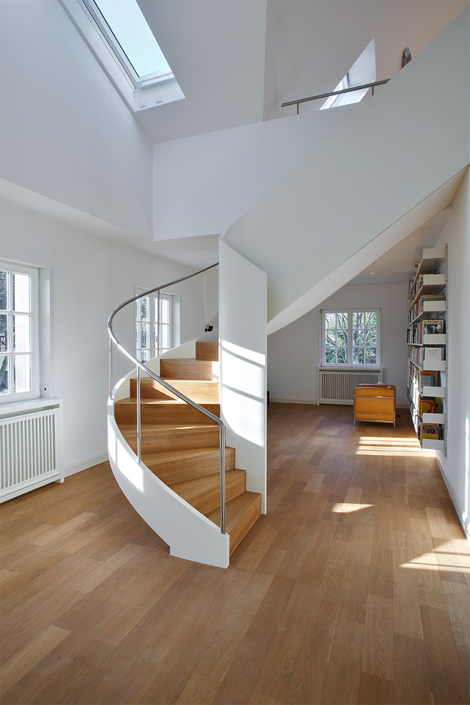 Large midcentury wood curved staircase in Cologne with wood risers and metal railing.