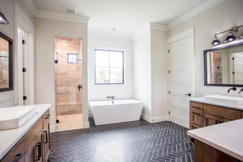 Large country master bathroom in Dallas with shaker cabinets, medium wood cabinets, a freestanding tub, an alcove shower, grey walls, porcelain floors, a vessel sink, quartzite benchtops, black floor, a hinged shower door and white benchtops.