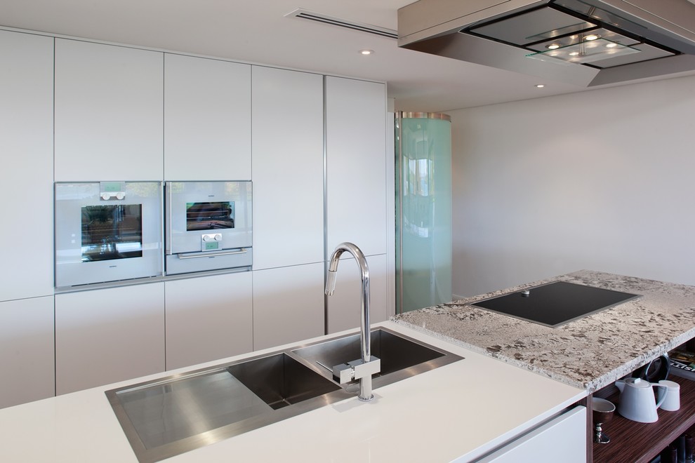 Photo of a large modern galley eat-in kitchen in Perth with a double-bowl sink, white cabinets, quartz benchtops, glass sheet splashback, stainless steel appliances, medium hardwood floors and with island.
