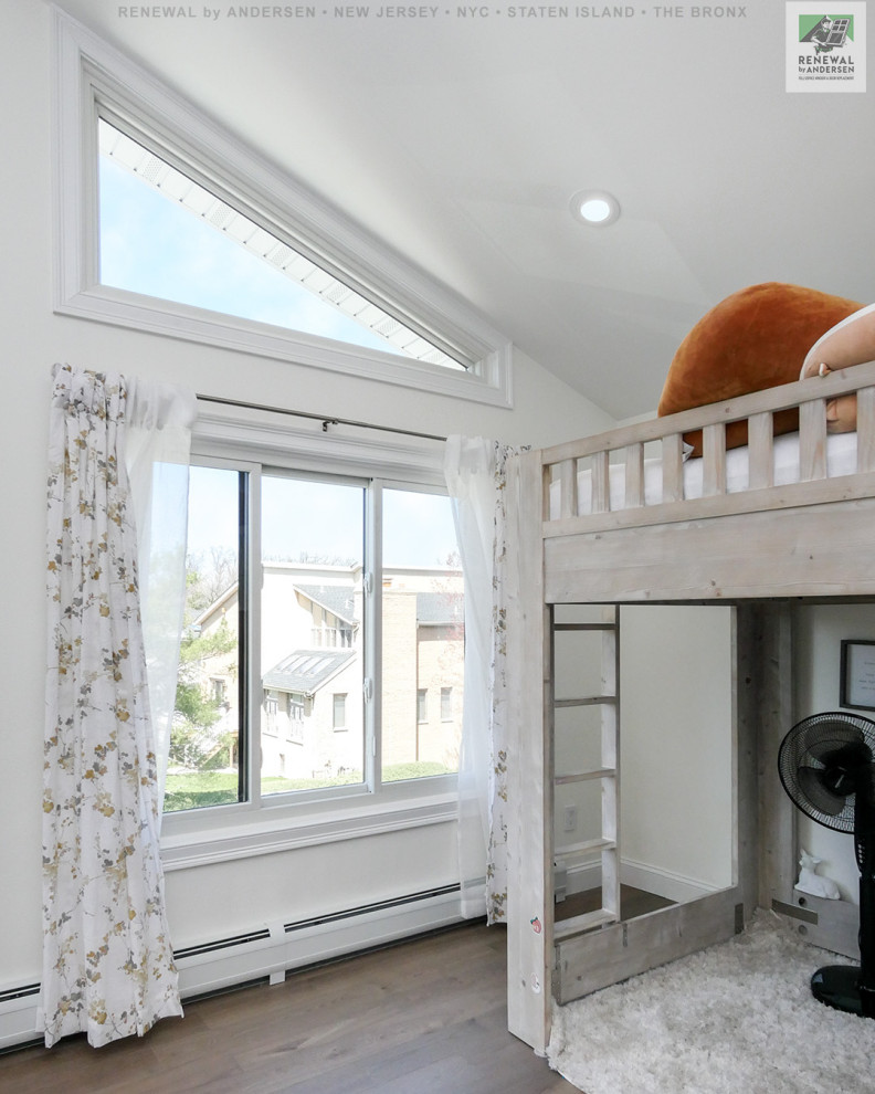 This is an example of a medium sized gender neutral children’s room in New York with white walls, medium hardwood flooring, brown floors and a vaulted ceiling.