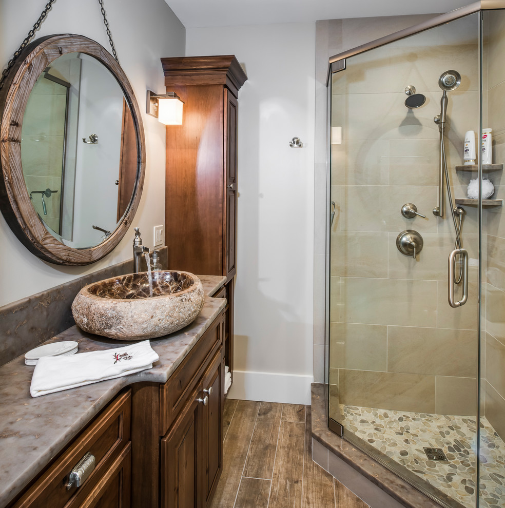 This is an example of a traditional master bathroom in Other with medium wood cabinets, a corner shower, beige tile, ceramic tile, beige walls, ceramic floors, a vessel sink, granite benchtops, brown floor, a hinged shower door and recessed-panel cabinets.