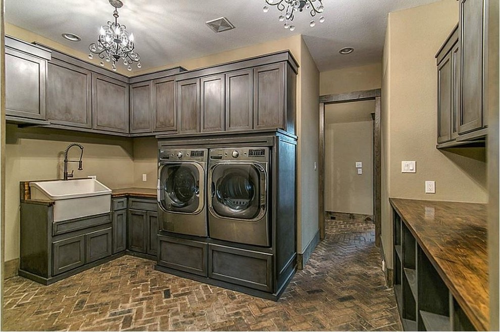 Photo of a large country u-shaped dedicated laundry room in Houston with a farmhouse sink, recessed-panel cabinets, grey cabinets, wood benchtops, beige walls, brick floors and a side-by-side washer and dryer.