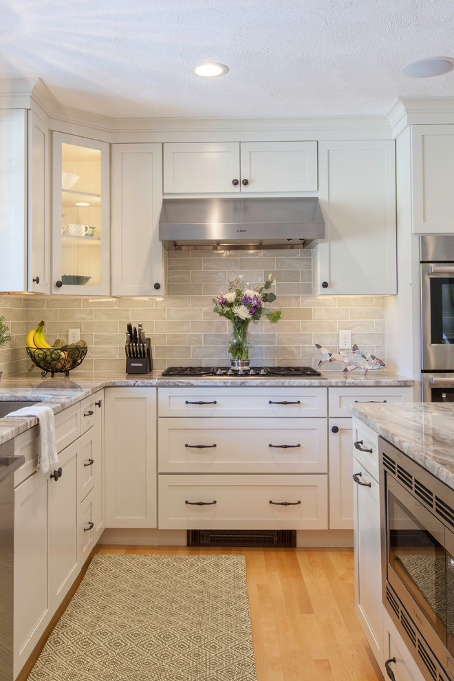 This is an example of a large transitional l-shaped eat-in kitchen in Boston with an undermount sink, shaker cabinets, white cabinets, granite benchtops, green splashback, glass tile splashback, stainless steel appliances, light hardwood floors and with island.