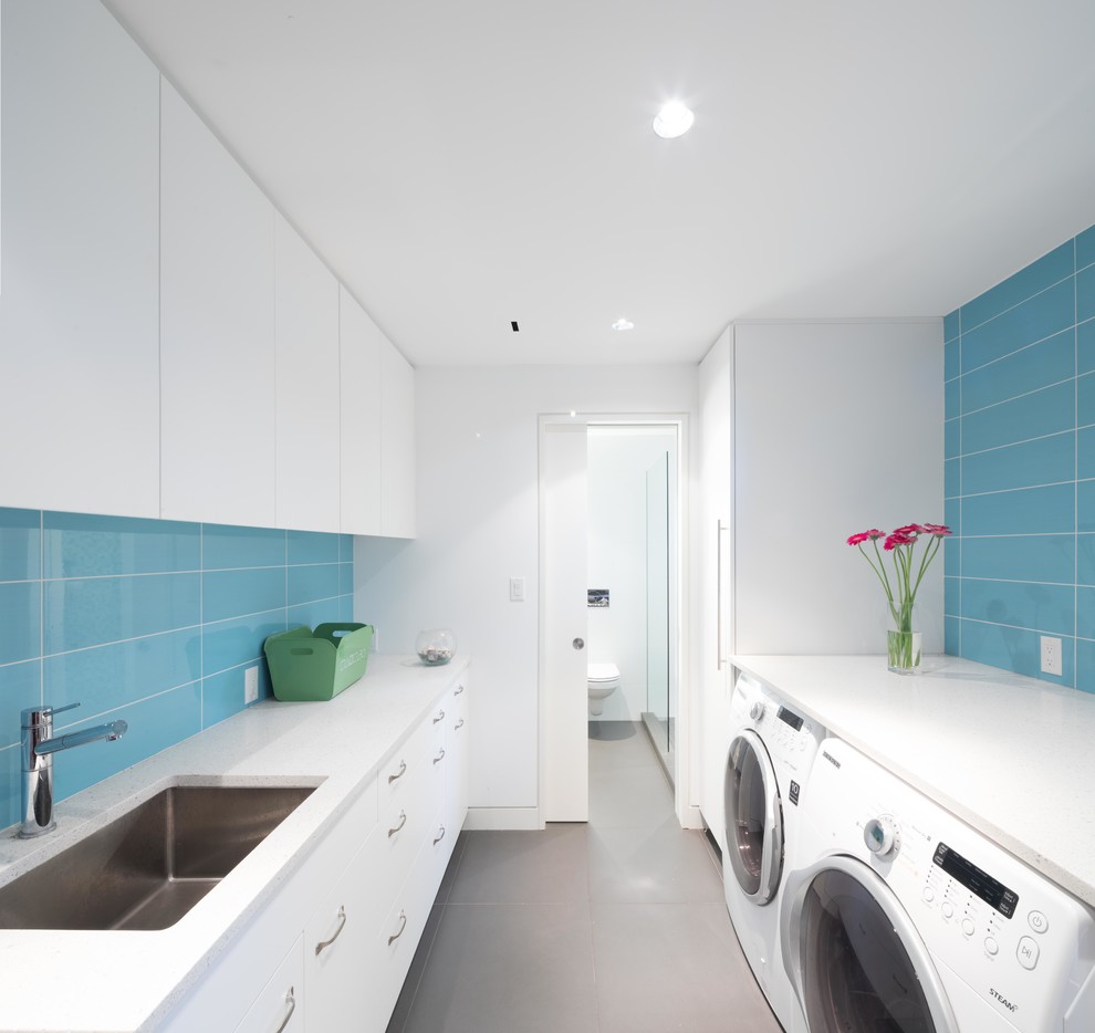 Design ideas for a contemporary galley dedicated laundry room in Vancouver with an undermount sink, flat-panel cabinets, white cabinets, white walls, a side-by-side washer and dryer, grey floor and white benchtop.