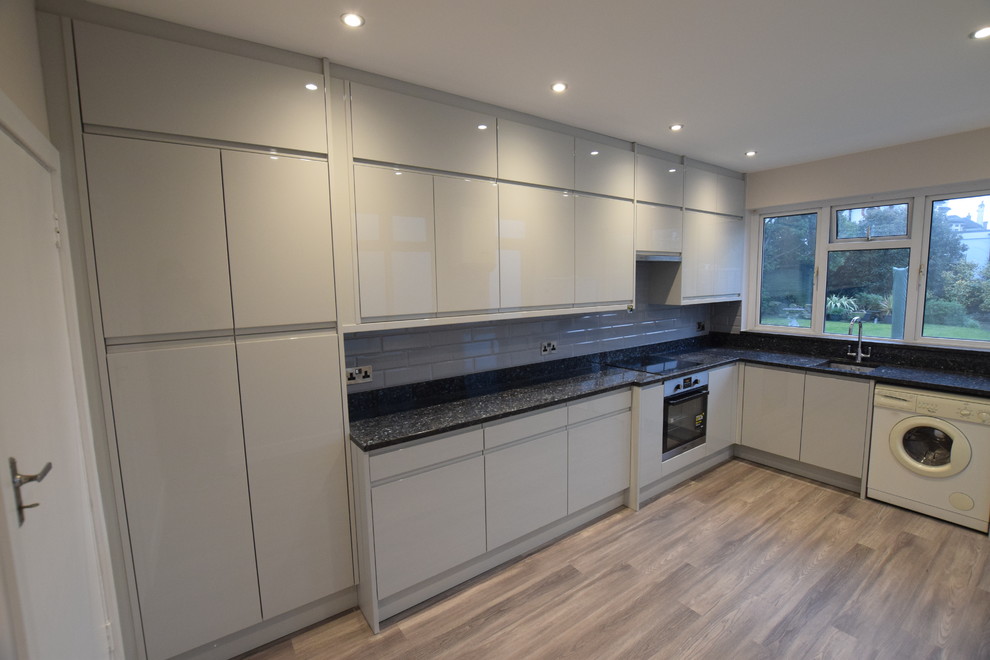 Design ideas for a mid-sized modern l-shaped eat-in kitchen in London with a single-bowl sink, beaded inset cabinets, grey cabinets, granite benchtops, grey splashback, ceramic splashback, stainless steel appliances, vinyl floors, no island, grey floor and black benchtop.