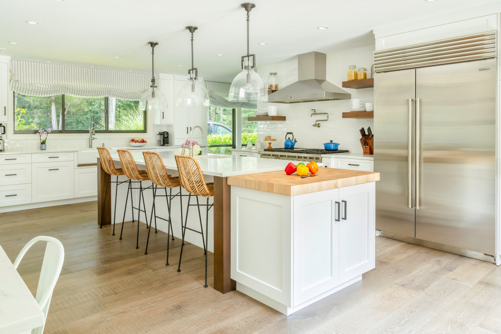 Inspiration for a large transitional u-shaped eat-in kitchen in New York with a farmhouse sink, shaker cabinets, white cabinets, quartzite benchtops, white splashback, ceramic splashback, stainless steel appliances, medium hardwood floors, with island, brown floor and white benchtop.