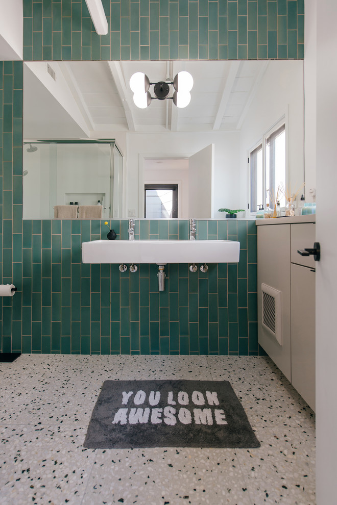 Photo of a small midcentury kids bathroom in Orange County with flat-panel cabinets, light wood cabinets, green tile, ceramic tile, green walls, terrazzo floors, a wall-mount sink, wood benchtops, multi-coloured floor and grey benchtops.