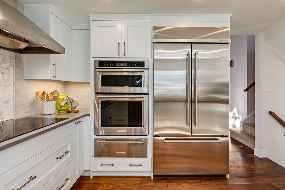 Inspiration for a mid-sized transitional l-shaped medium tone wood floor enclosed kitchen remodel in Calgary with an undermount sink, recessed-panel cabinets, white cabinets, quartz countertops, gray backsplash, porcelain backsplash, stainless steel appliances and an island