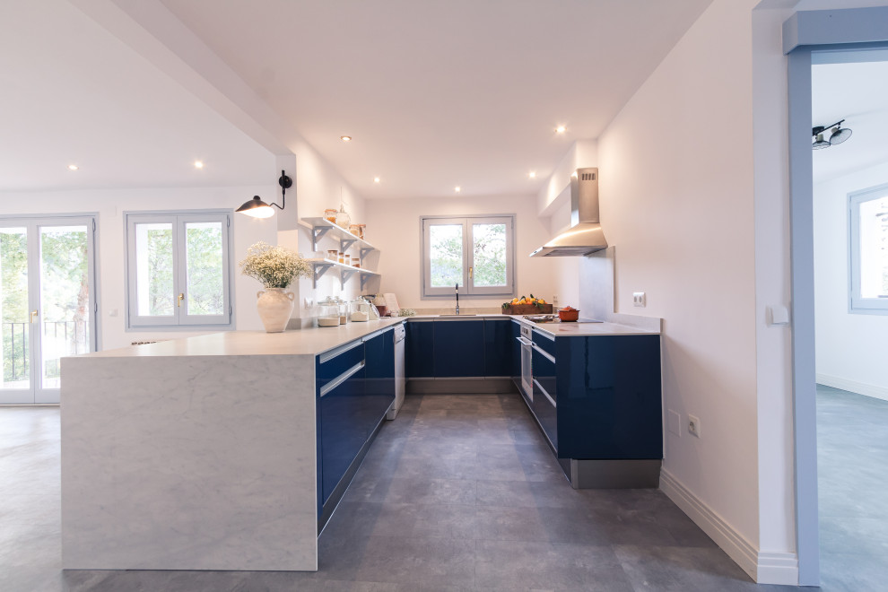 Photo of a large mediterranean u-shaped kitchen in Barcelona with an undermount sink, flat-panel cabinets, blue cabinets, white splashback, white appliances, vinyl floors, a peninsula, grey floor and white benchtop.