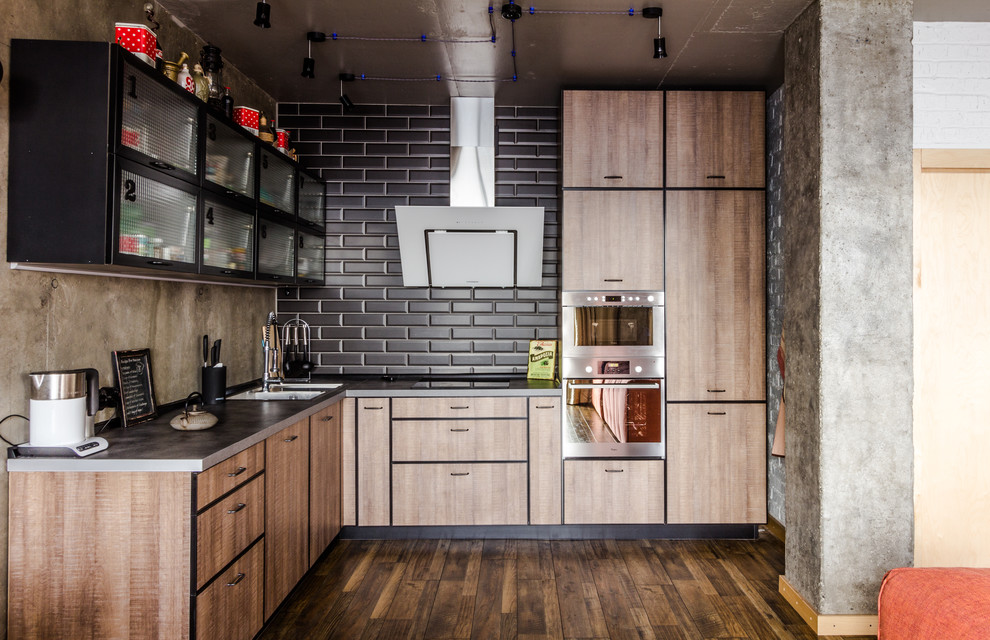 Photo of an industrial l-shaped open plan kitchen in Other with flat-panel cabinets, medium wood cabinets, black splashback, subway tile splashback, stainless steel appliances, dark hardwood floors, no island, brown floor, a double-bowl sink and stainless steel benchtops.