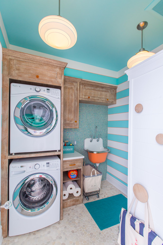 This is an example of a mid-sized eclectic single-wall dedicated laundry room in Philadelphia with a farmhouse sink, recessed-panel cabinets, quartz benchtops, blue walls, a stacked washer and dryer, porcelain floors, beige floor and medium wood cabinets.