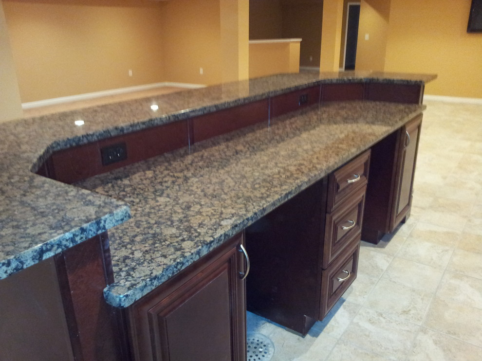 This is an example of a large traditional single-wall seated home bar in St Louis with an undermount sink, raised-panel cabinets, dark wood cabinets, granite benchtops and ceramic floors.