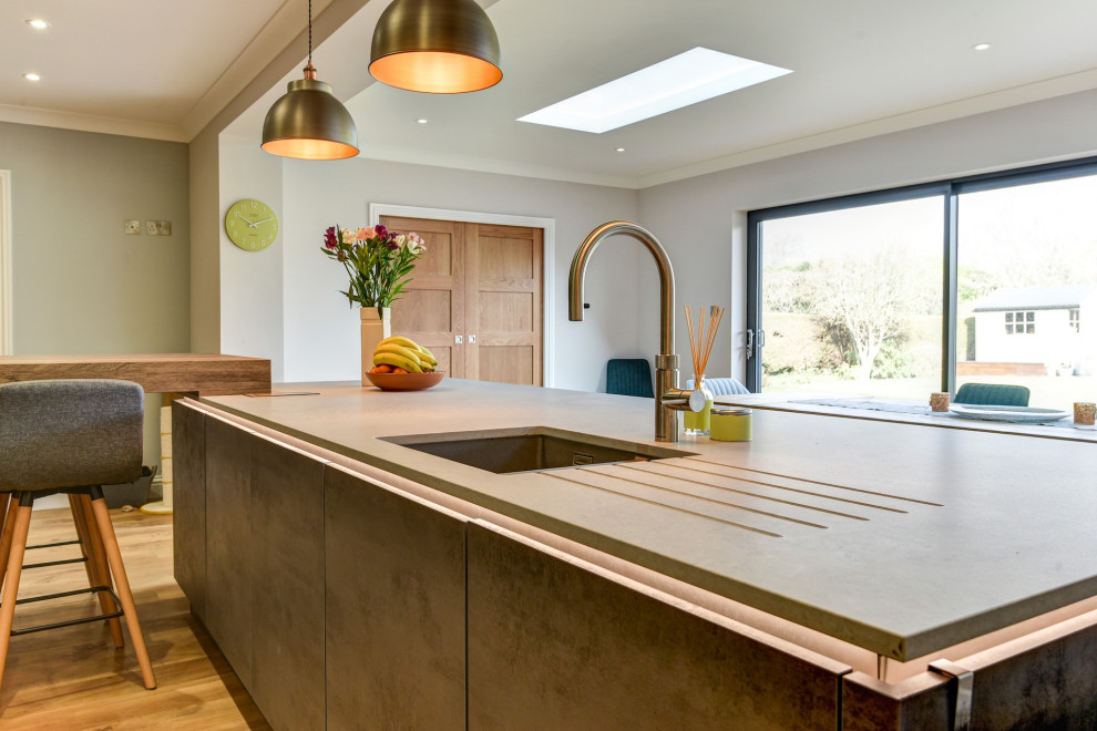 Photo of a large modern grey and white galley kitchen/diner in Sussex with a submerged sink, flat-panel cabinets, medium wood cabinets, quartz worktops, multi-coloured splashback, ceramic splashback, black appliances, light hardwood flooring, multiple islands, brown floors, white worktops and feature lighting.