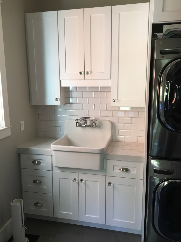 Mid-sized arts and crafts single-wall dedicated laundry room in Orlando with a farmhouse sink, shaker cabinets, white cabinets, quartz benchtops, grey walls, porcelain floors, a stacked washer and dryer, grey floor and white benchtop.