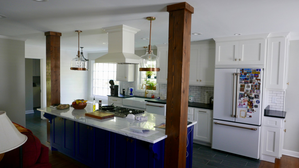 Example of a mid-sized transitional galley porcelain tile and black floor eat-in kitchen design with a farmhouse sink, shaker cabinets, blue cabinets, marble countertops, white backsplash, subway tile backsplash, white appliances, an island and multicolored countertops