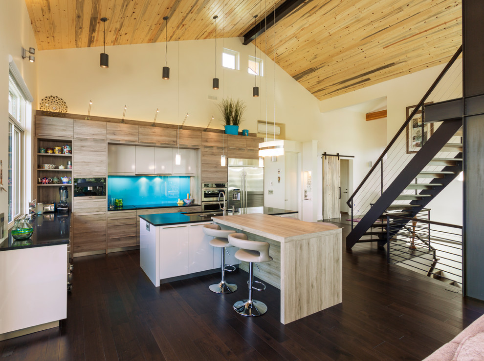 This is an example of a mid-sized modern l-shaped eat-in kitchen in Denver with a drop-in sink, flat-panel cabinets, light wood cabinets, onyx benchtops, blue splashback, stainless steel appliances, dark hardwood floors and multiple islands.