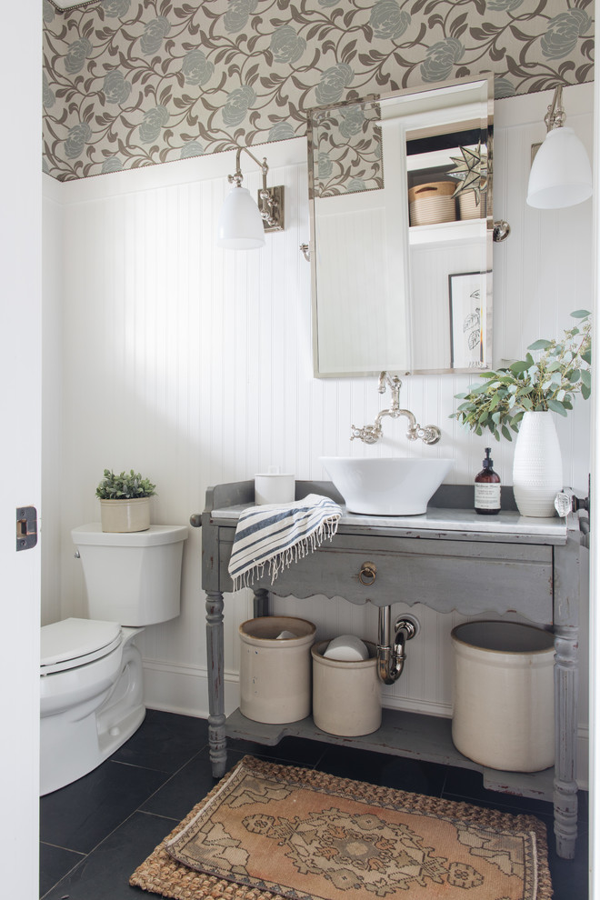 Inspiration for a transitional powder room in Chicago with furniture-like cabinets, grey cabinets, a two-piece toilet, multi-coloured walls, a vessel sink, black floor and white benchtops.