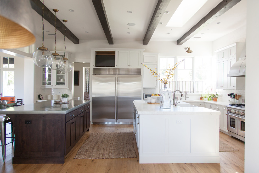 Eat-in kitchen - large transitional l-shaped light wood floor eat-in kitchen idea in Phoenix with a farmhouse sink, white cabinets, white backsplash, stainless steel appliances, an island, shaker cabinets, stainless steel countertops and porcelain backsplash