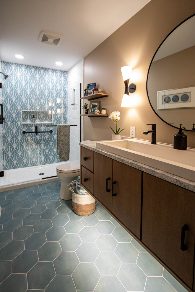 This is an example of a mid-sized transitional 3/4 bathroom in Cleveland with furniture-like cabinets, brown cabinets, an alcove shower, a two-piece toilet, beige tile, porcelain tile, blue walls, porcelain floors, a trough sink, engineered quartz benchtops, blue floor, a hinged shower door, beige benchtops, a niche, a single vanity and a floating vanity.