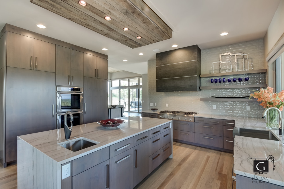 Mid-sized modern l-shaped eat-in kitchen in Denver with a farmhouse sink, flat-panel cabinets, grey cabinets, quartzite benchtops, glass tile splashback, stainless steel appliances, light hardwood floors, with island, grey floor and white benchtop.