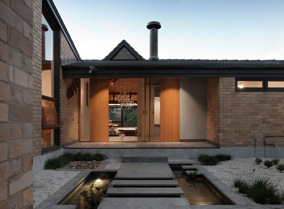 This is an example of an expansive midcentury two-storey beige house exterior in Sydney with concrete fiberboard siding, a hip roof and a tile roof.