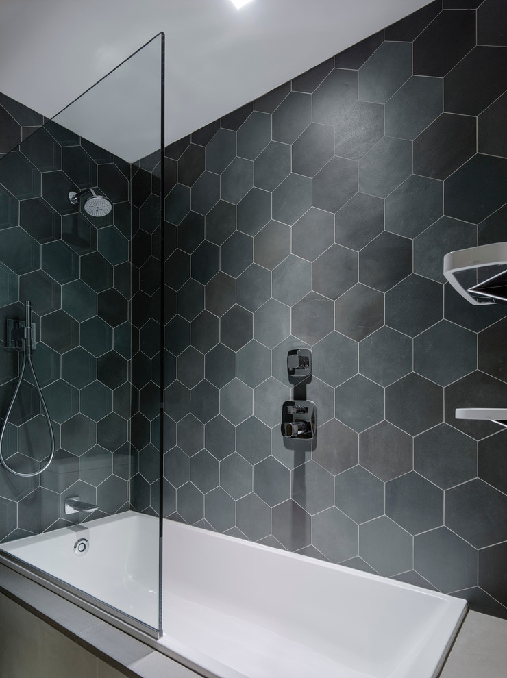 Photo of a modern bathroom in New York with an alcove tub, a shower/bathtub combo, black tile, gray tile, ceramic tile and black walls.