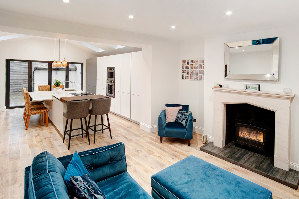 Photo of a modern kitchen with flat-panel cabinets, white cabinets, quartz worktops, stainless steel appliances, medium hardwood flooring, an island and white worktops.