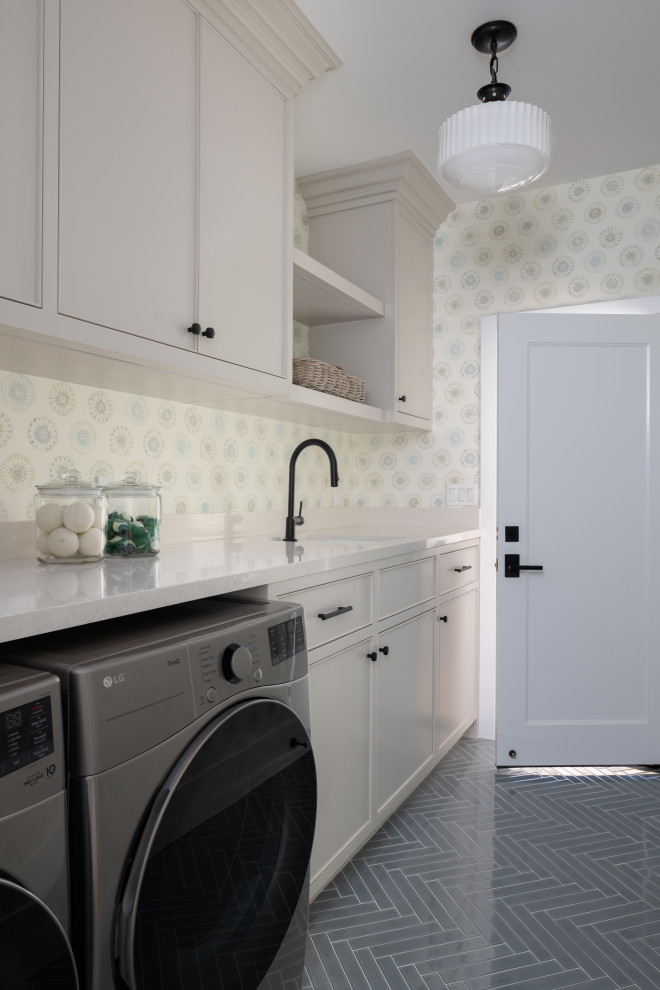 Inspiration for a large beach style galley dedicated laundry room in Orange County with an undermount sink, beaded inset cabinets, grey cabinets, quartz benchtops, white splashback, engineered quartz splashback, multi-coloured walls, porcelain floors, a side-by-side washer and dryer, blue floor, white benchtop and wallpaper.