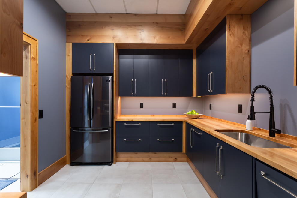 Photo of a small industrial l-shaped separate kitchen in Milwaukee with an undermount sink, flat-panel cabinets, black cabinets, wood benchtops, brown splashback, timber splashback, black appliances, porcelain floors, no island, white floor and brown benchtop.