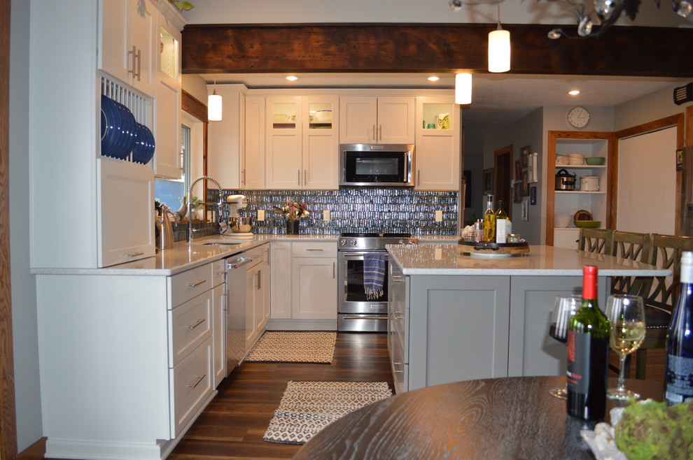Inspiration for a mid-sized transitional l-shaped brown floor eat-in kitchen remodel with a double-bowl sink, shaker cabinets, white cabinets, quartzite countertops, multicolored backsplash, glass tile backsplash, stainless steel appliances, an island and white countertops