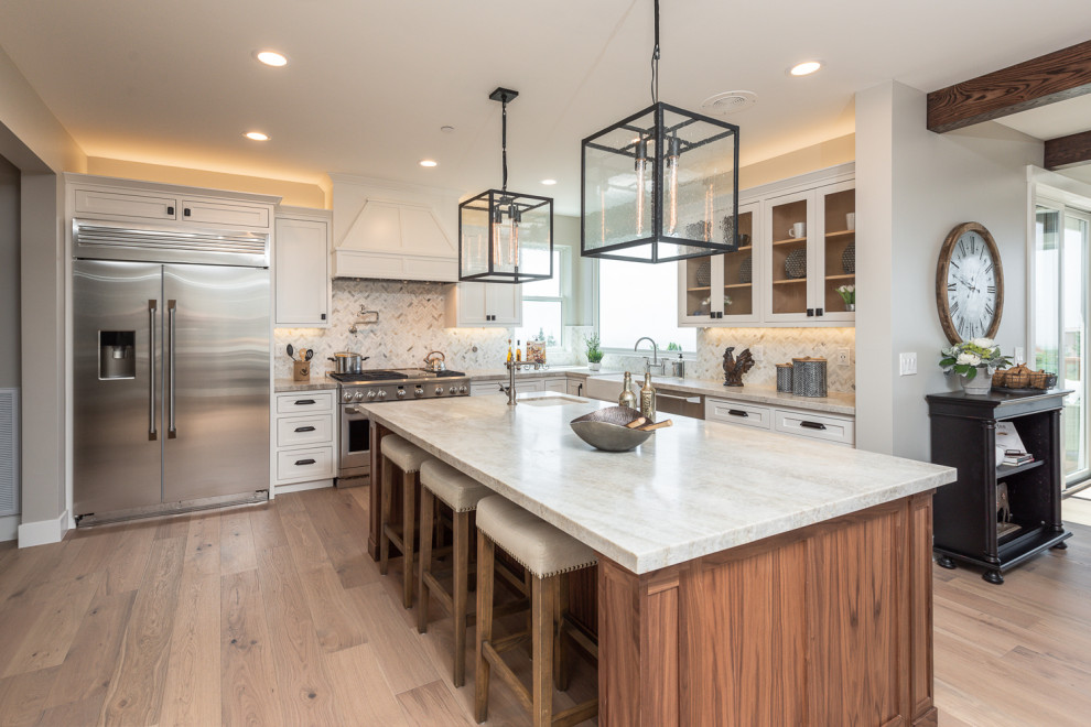 Photo of a transitional l-shaped kitchen in San Francisco with a farmhouse sink, shaker cabinets, white cabinets, white splashback, stainless steel appliances, medium hardwood floors, with island, brown floor and white benchtop.