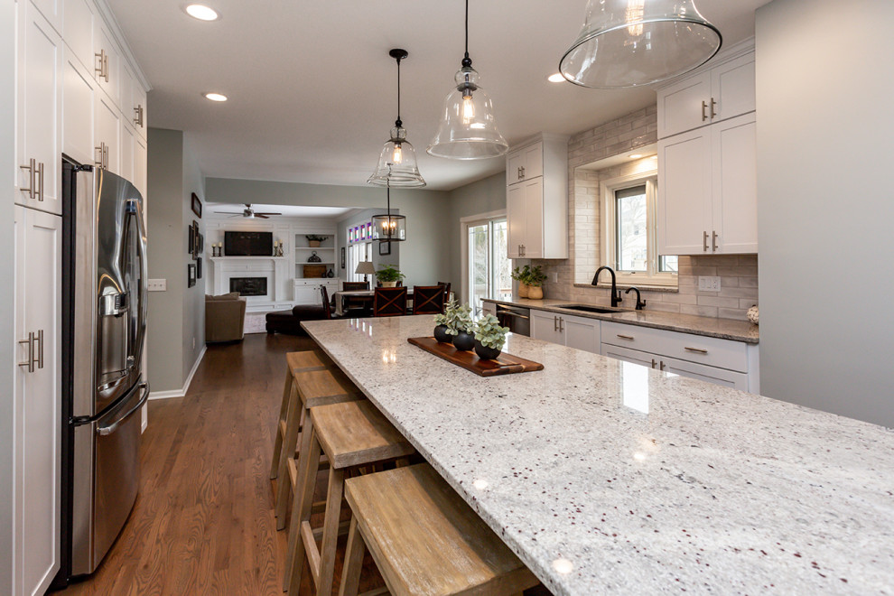 Inspiration for a large transitional u-shaped medium tone wood floor and brown floor eat-in kitchen remodel with an undermount sink, recessed-panel cabinets, white cabinets, granite countertops, white backsplash, subway tile backsplash, stainless steel appliances, an island and gray countertops