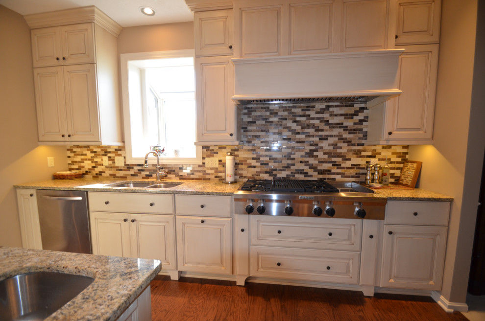 Eat-in kitchen - mid-sized transitional u-shaped medium tone wood floor and brown floor eat-in kitchen idea with an undermount sink, raised-panel cabinets, beige cabinets, granite countertops, multicolored backsplash, mosaic tile backsplash, stainless steel appliances, an island and multicolored countertops