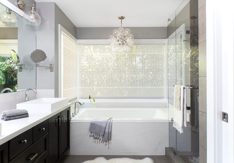 Photo of a mid-sized contemporary 3/4 bathroom in San Francisco with shaker cabinets, black cabinets, a drop-in tub, grey walls, a vessel sink, grey floor, a hinged shower door, white benchtops, an alcove shower, white tile, stone slab, porcelain floors and solid surface benchtops.