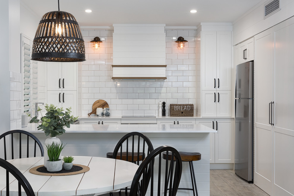 Beach style l-shaped eat-in kitchen in Sunshine Coast with a drop-in sink, shaker cabinets, white cabinets, white splashback, subway tile splashback, stainless steel appliances, a peninsula, grey floor and white benchtop.