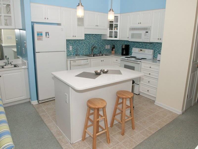 This is an example of a mid-sized beach style l-shaped eat-in kitchen in Raleigh with a double-bowl sink, white cabinets, blue splashback, glass tile splashback, white appliances and with island.