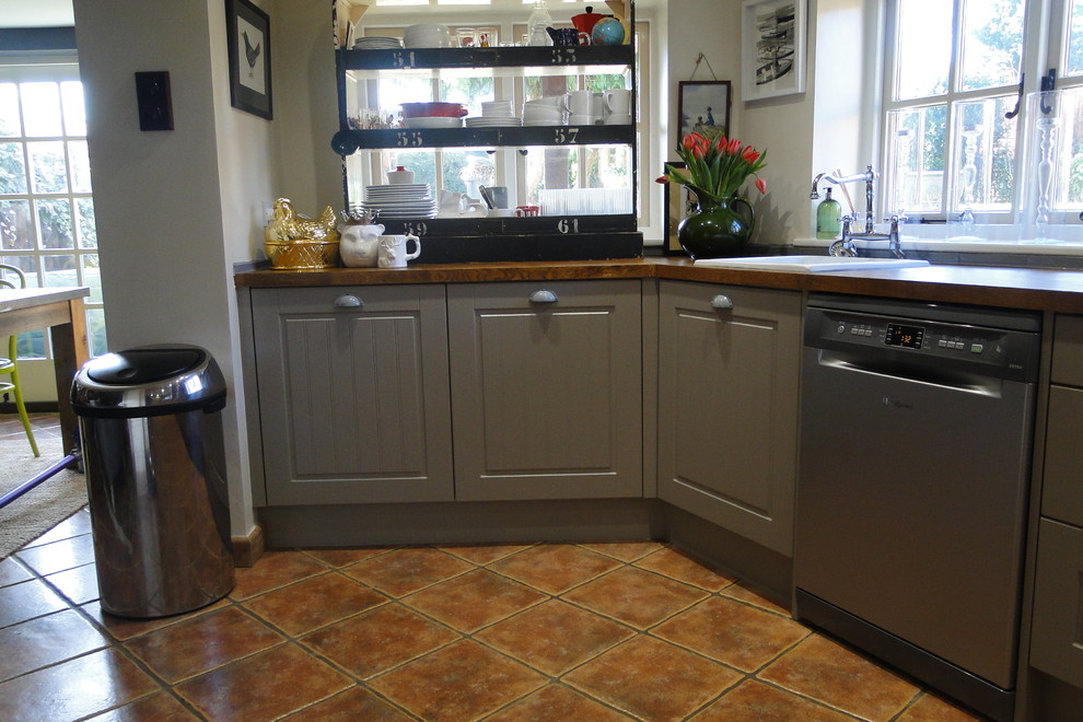 This is an example of a mid-sized country l-shaped open plan kitchen in Other with a drop-in sink, raised-panel cabinets, grey cabinets, wood benchtops, ceramic splashback, stainless steel appliances and terra-cotta floors.