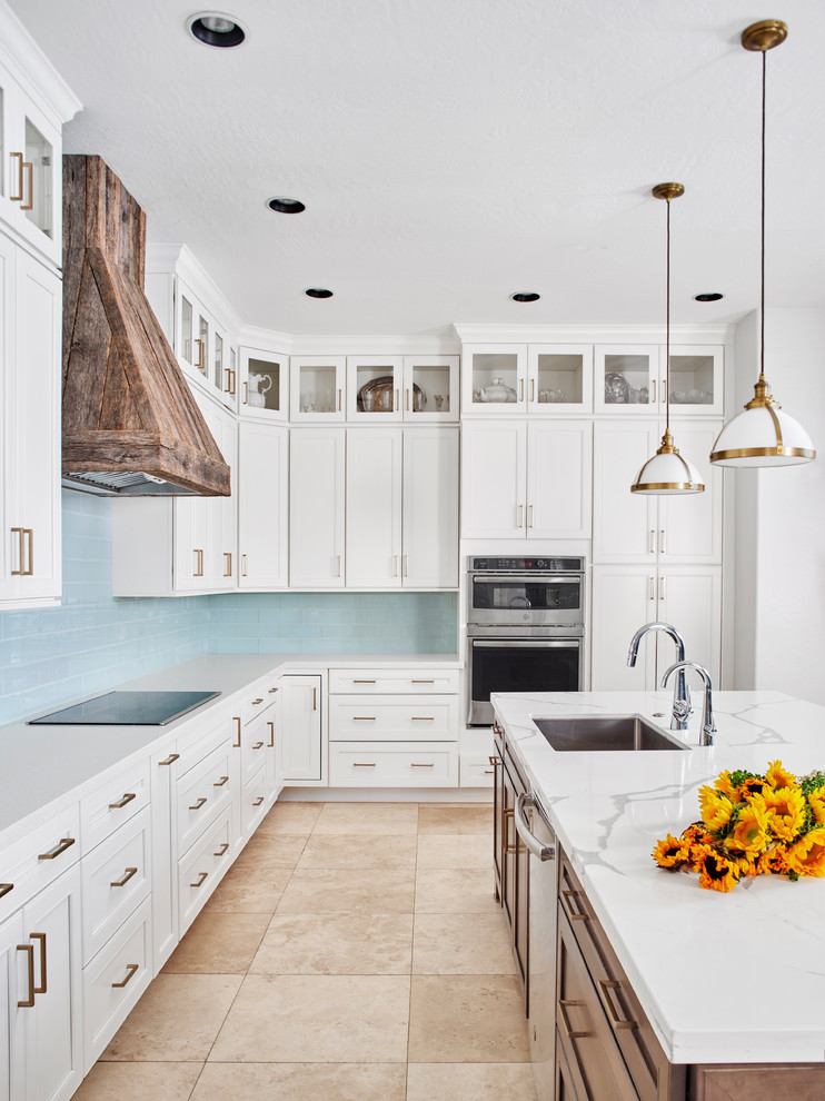 Expansive transitional l-shaped open plan kitchen in Phoenix with an undermount sink, recessed-panel cabinets, white cabinets, quartz benchtops, blue splashback, porcelain splashback, stainless steel appliances, travertine floors, with island, beige floor and white benchtop.