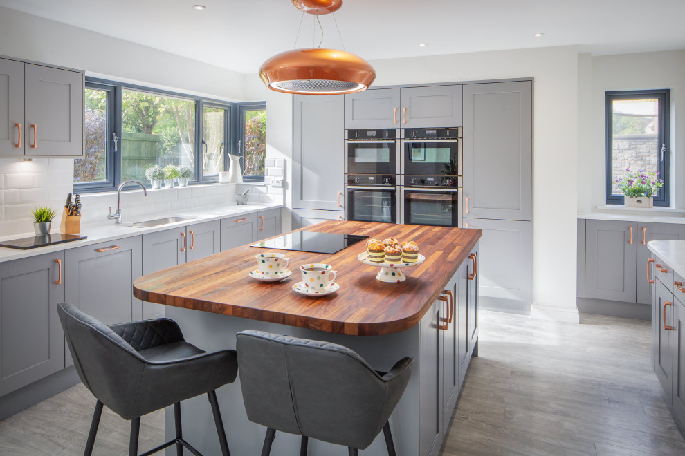 Large transitional u-shaped eat-in kitchen in Other with an undermount sink, shaker cabinets, grey cabinets, wood benchtops, white splashback, ceramic splashback, black appliances, vinyl floors, with island, grey floor and white benchtop.