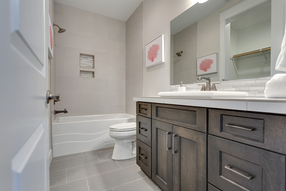 Photo of a large transitional master bathroom in Portland with recessed-panel cabinets, dark wood cabinets, a two-piece toilet, gray tile, porcelain tile, grey walls, porcelain floors, an undermount sink, an alcove tub, a shower/bathtub combo and tile benchtops.