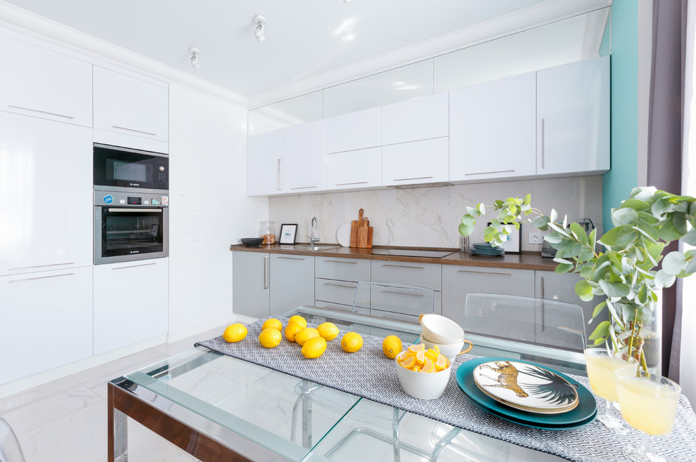 Mid-sized contemporary l-shaped eat-in kitchen in Novosibirsk with a drop-in sink, flat-panel cabinets, white cabinets, laminate benchtops, white splashback, porcelain splashback, stainless steel appliances, porcelain floors, no island, white floor and brown benchtop.