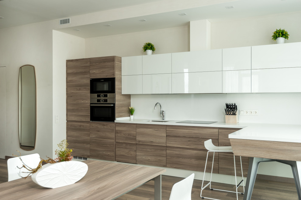 Photo of a large modern l-shaped kitchen/diner in Los Angeles with a built-in sink, flat-panel cabinets, white cabinets, wood worktops, white splashback, granite splashback, stainless steel appliances, light hardwood flooring, multiple islands and white worktops.
